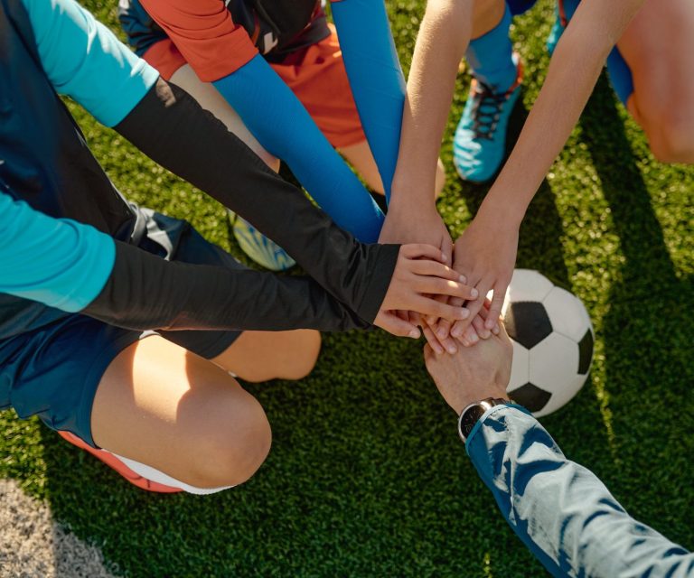 Junge Fußballmannschaft feiert zusammen mit ihrem Trainer und legt die Hände in die Mitte.
